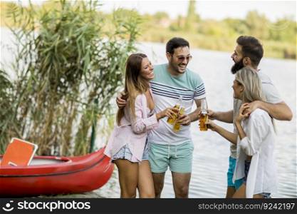 Group of friends with cider bottles standing by the boat near the beautiful lake and having fun on a summer day