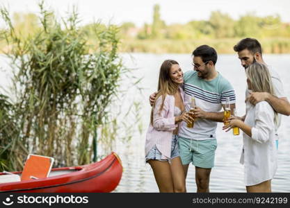 Group of friends with cider bottles standing by the boat near the beautiful lake and having fun on a summer day