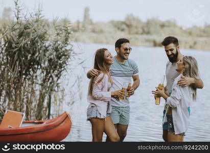 Group of friends with cider bottles standing by the boat near the beautiful lake and having fun on a summer day