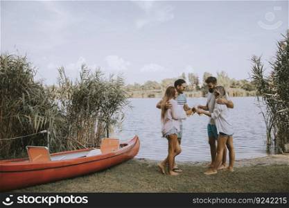 Group of friends with cider bottles standing by the boat near the beautiful lake and having fun on a summer day