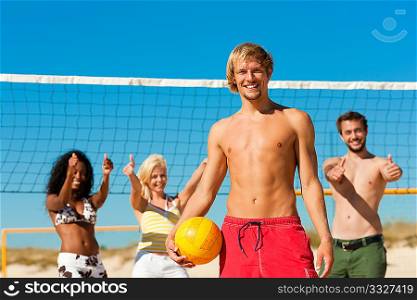 Group of friends - women and men - playing beach volleyball, one in front having the ball
