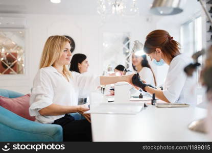 Group of girlfriends relax on manicure procedure in beauty salon. Professional beautician and female customers, nail care in spa, fingernail treatment. Group of girlfriends, manicure in beauty salon