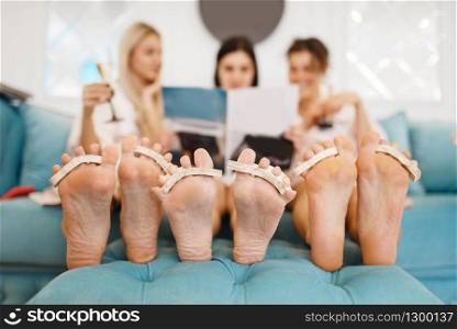 Group of girlfriends relax on pedicure procedure in beauty salon. Professional beautician and female customers, nail care in spa studio, toenail treatment