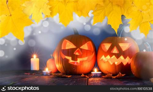 Group of Halloween pumpkin head jack o lantern and candles on dark wooden background , bokeh lights and autumn yellow maple leaves frame. Halloween pumpkin and candles