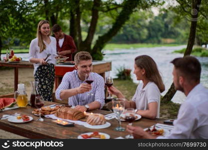 group of happy friends having picnic french dinner party outdoor during summer holiday vacation near the river at beautiful nature