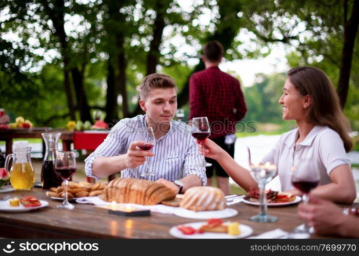 group of happy friends having picnic french dinner party outdoor during summer holiday vacation  near the river at beautiful nature