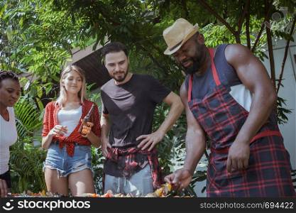 Group of happy friends standing eating and drinking beers at barbecue dinner camping in nature and having meal together outdoor as summer lifestyle, food and friendship concept