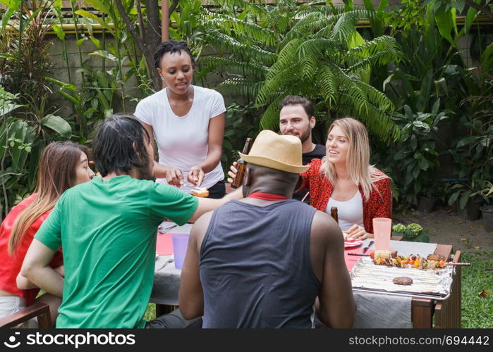 Group of happy friends standing eating and drinking beers at barbecue dinner camping in nature and having meal together outdoor as summer lifestyle, food and friendship concept