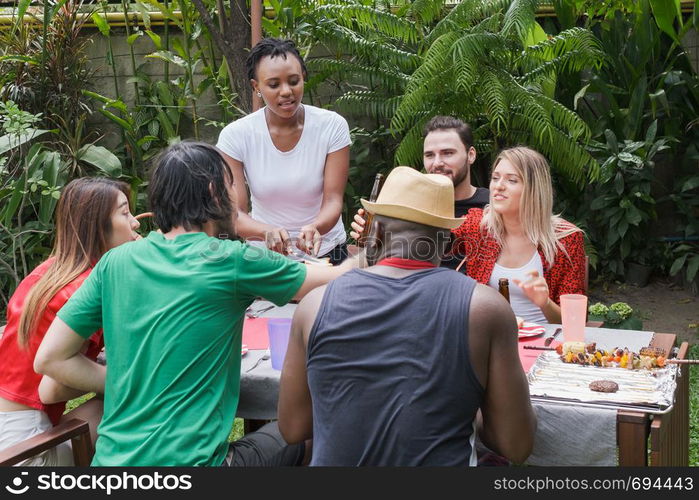 Group of happy friends standing eating and drinking beers at barbecue dinner camping in nature and having meal together outdoor as summer lifestyle, food and friendship concept