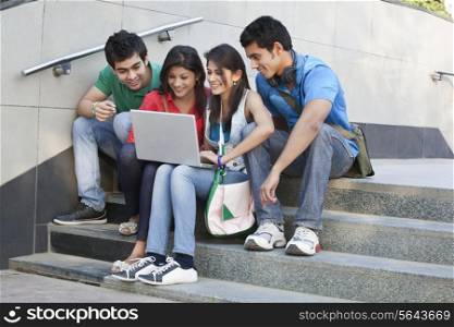 Group of happy friends surfing net while sitting on steps