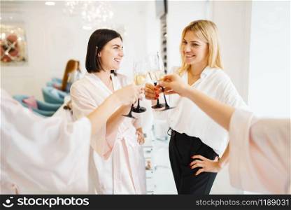 Group of happy girlfriends clink glasses in beauty salon. Professional beautician service. Female customers celebrate the meeting in spa studio. Group of girlfriends clink glasses in beauty salon