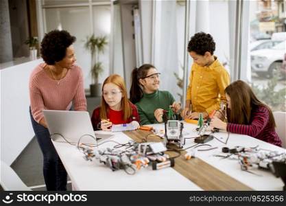 Group of happy kids with their African American fema≤science teacher with laptop programming e≤ctric toys and robots at robotics classroom