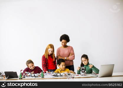 Group of happy kids with their African American female science teacher programming electric toys and robots at robotics classroom