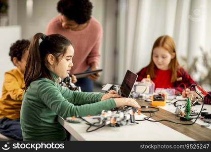 Group of happy kids with their African American female science teacher with laptop programming electric toys and robots at robotics classroom