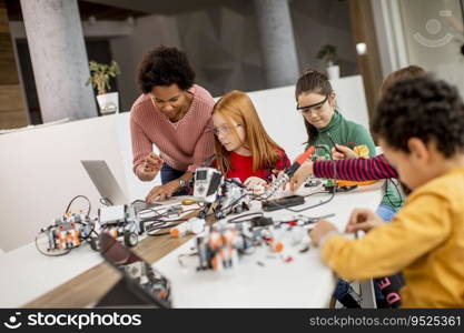 Group of happy kids with their African American female science teacher with laptop programming electric toys and robots at robotics classroom