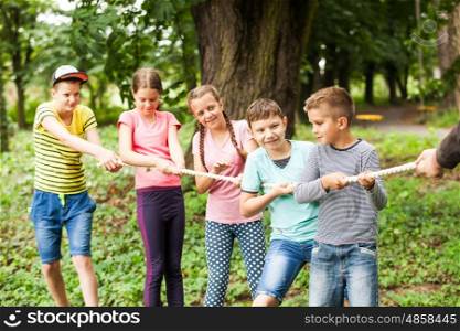 Group of happy smiling kids playing tug-of-war with rope in green park,