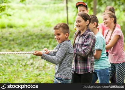 Group of happy smiling kids playing tug-of-war with rope in green park,