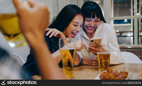 Group of happy tourist young Asia friend using mobile phone, drink alcohol beer and having hangout party in night club at Khao San Road. Traveler backpacker Asia people travel in Bangkok, Thailand.