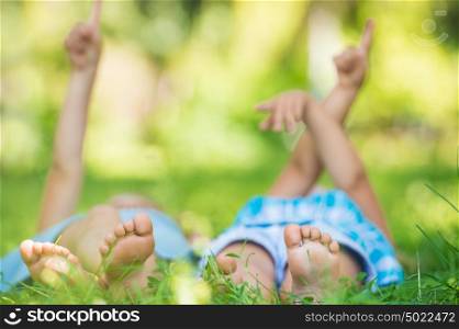 Group of happy unrecognizable children lying on green grass and pointing to the sky outdoors in summer park