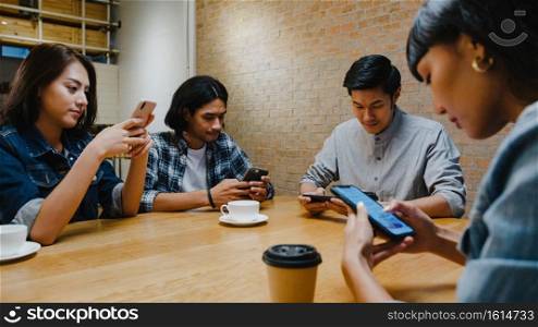 Group of happy young Asia friends having fun a great time and using smartphone together while sitting together at cafe restaurant. Coffee shop holiday activity, modern friendship lifestyle concept.