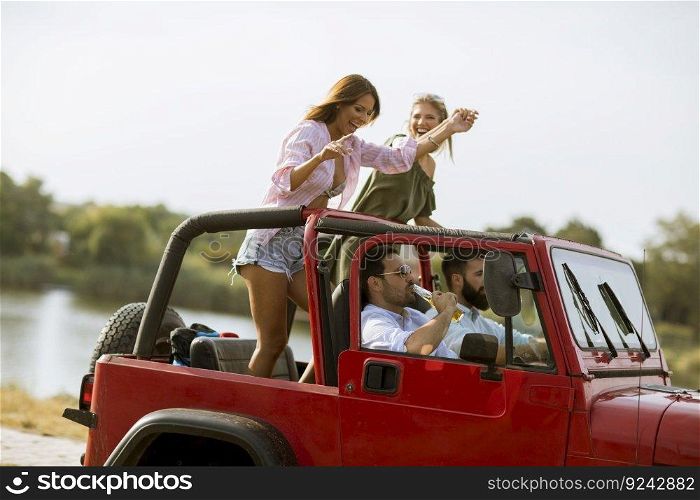 Group of happy young friends having fun in convertible car during summer vacation by river