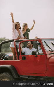 Group of happy young friends having fun in convertible car during summer vacation by river