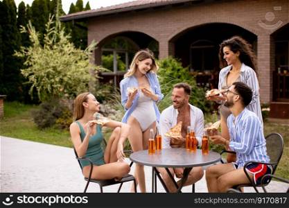 Group of happy young people cheering with cider and eating pizza by the pool in the garden