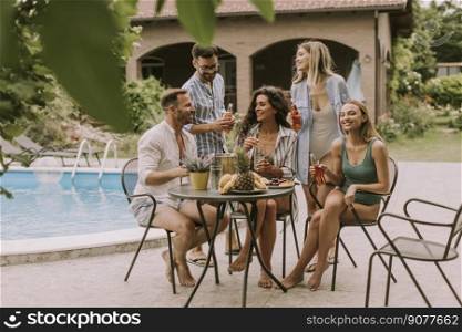Group of happy young people cheering with cider by the pool in the garden