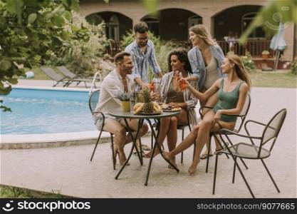 Group of happy young people cheering with cider by the pool in the garden