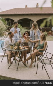 Group of happy young people cheering with cider by the pool in the garden