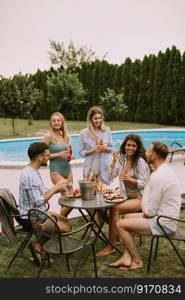 Group of happy young people cheering with cider by the pool in the garden