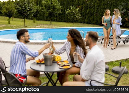 Group of happy young people cheering with drinks and eating fruits by the pool in the garden