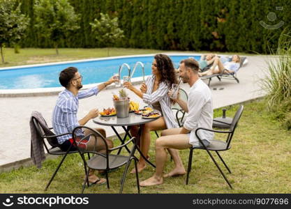 Group of happy young people cheering with drinks and eating fruits by the pool in the garden