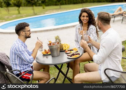 Group of happy young people cheering with drinks and eating fruits by the pool in the garden