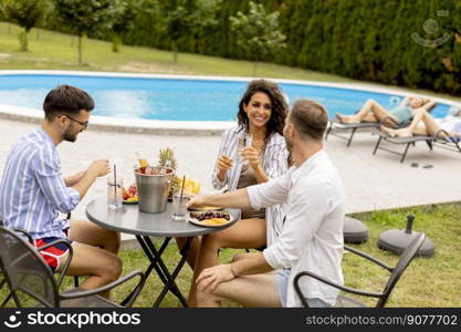 Group of happy young people cheering with drinks and eating fruits by the pool in the garden