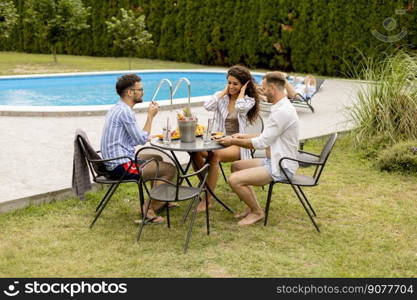 Group of happy young people cheering with drinks and eating fruits by the pool in the garden