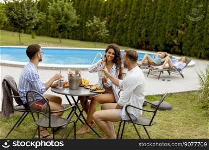 Group of happy young people cheering with drinks and eating fruits by the pool in the garden
