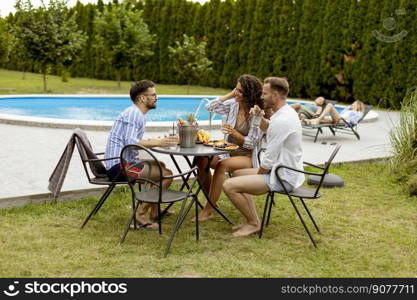 Group of happy young people cheering with drinks and eating fruits by the pool in the garden