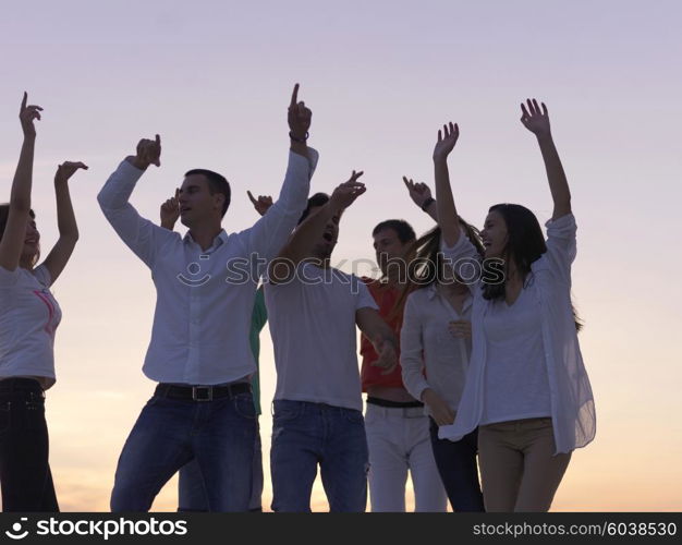 group of happy young people dancing and have fun on party in modern home bacony with sunset and ocean in background