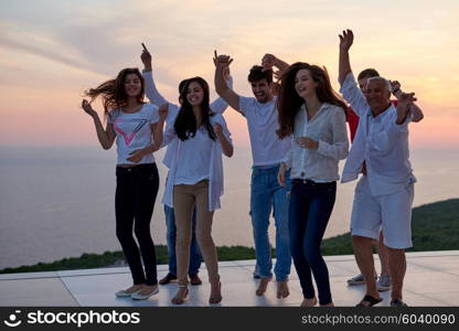 group of happy young people dancing and have fun on party in modern home bacony with sunset and ocean in background