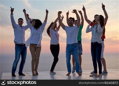 group of happy young people dancing and have fun on party in modern home bacony with sunset and ocean in background