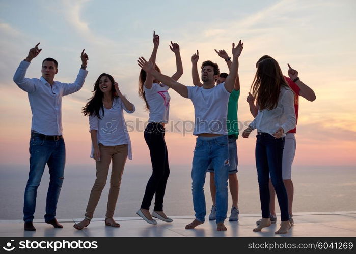 group of happy young people dancing and have fun on party in modern home bacony with sunset and ocean in background