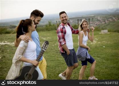 Group of happy young people with acoustic guitar walking in the summer field