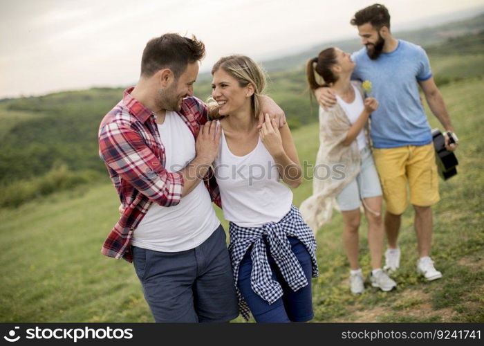 Group of happy young people with acoustic guitar walking in the summer field