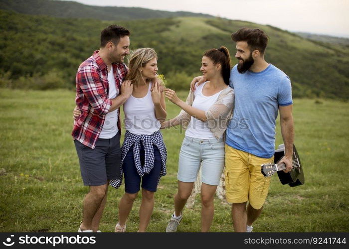 Group of happy young people with acoustic guitar walking in the summer field