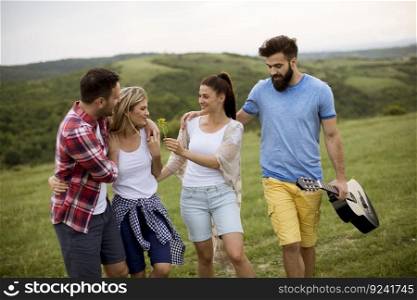 Group of happy young people with acoustic guitar walking in the summer field