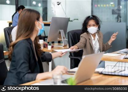 Group of interracial business worker team wear protective face mask in new normal office with social distance practice with hand sanitiser alcohol gel on table prevent coronavirus COVID-19 spreading