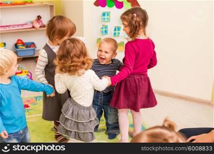 Group of little children dancing holding hands and enthusiastically watching the boy, who laughs with joy