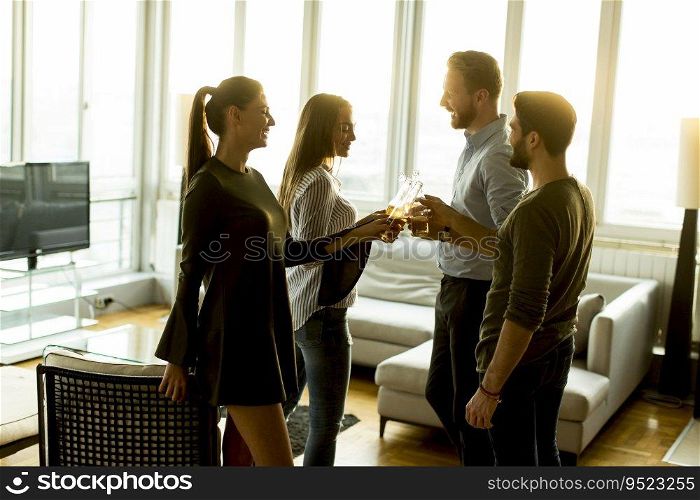 Group of male and female friends having fun at home and toasting with cider bottles
