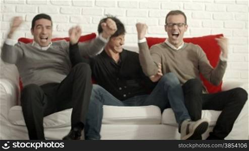 Group of male friends watching sport game on TV at home and having fun. Dolly shot